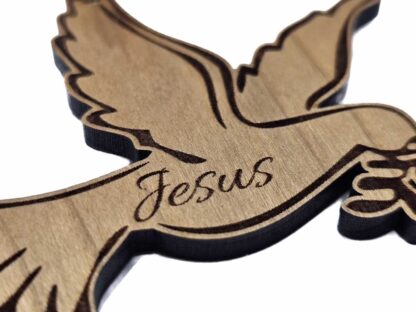Nahaufnahme einer Holztaube mit präziser Lasergravur des Wortes "Jesus". Die natürliche Maserung des Holzes ist deutlich sichtbar.