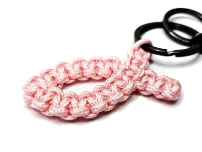 Nahaufnahme eines handgeknüpften Ichthys-Fisch-Schlüsselanhängers aus rosa Paracord mit zwei Schlüsselringen und Mini-Karabiner.